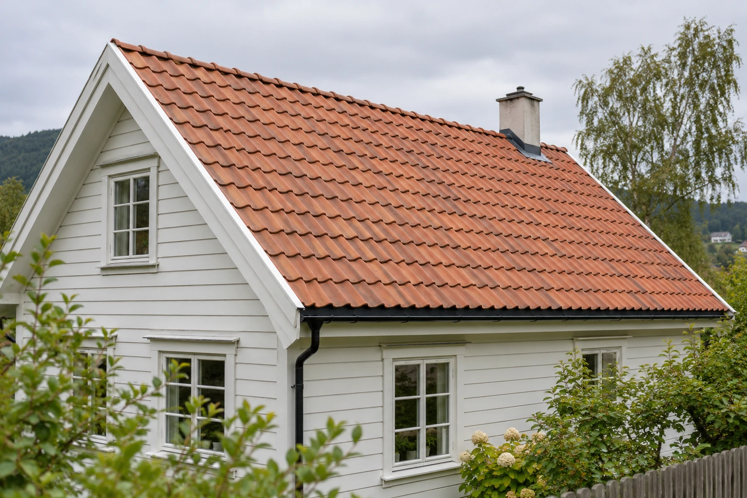 Hvitt trehus med eldre rødt tegltak og pipe